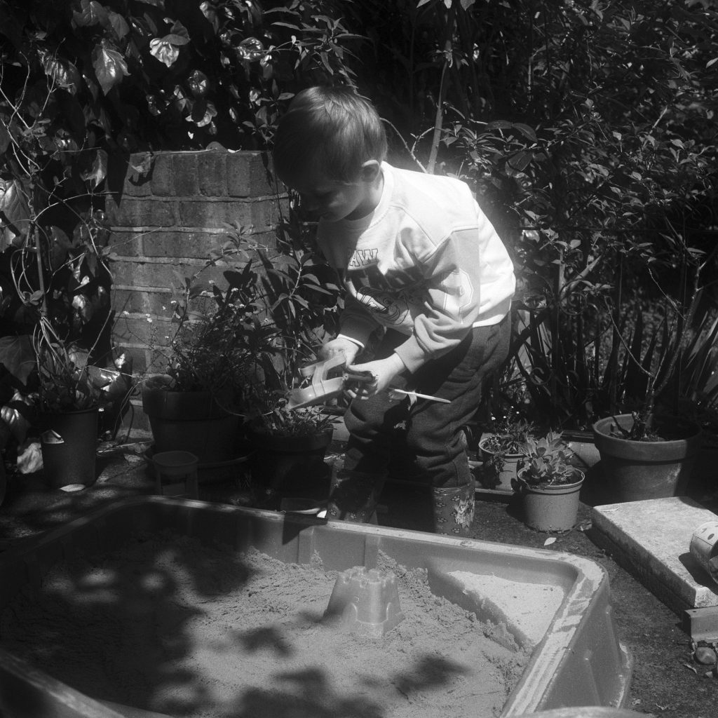 An scanned black and white image of a boy playing in a sand pit from 120 film, showing some glowing of the highlights