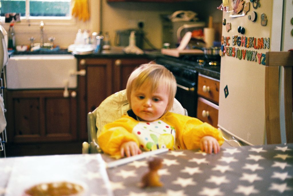 A colour photo of a young child sat in a high chair showing very saturated colours