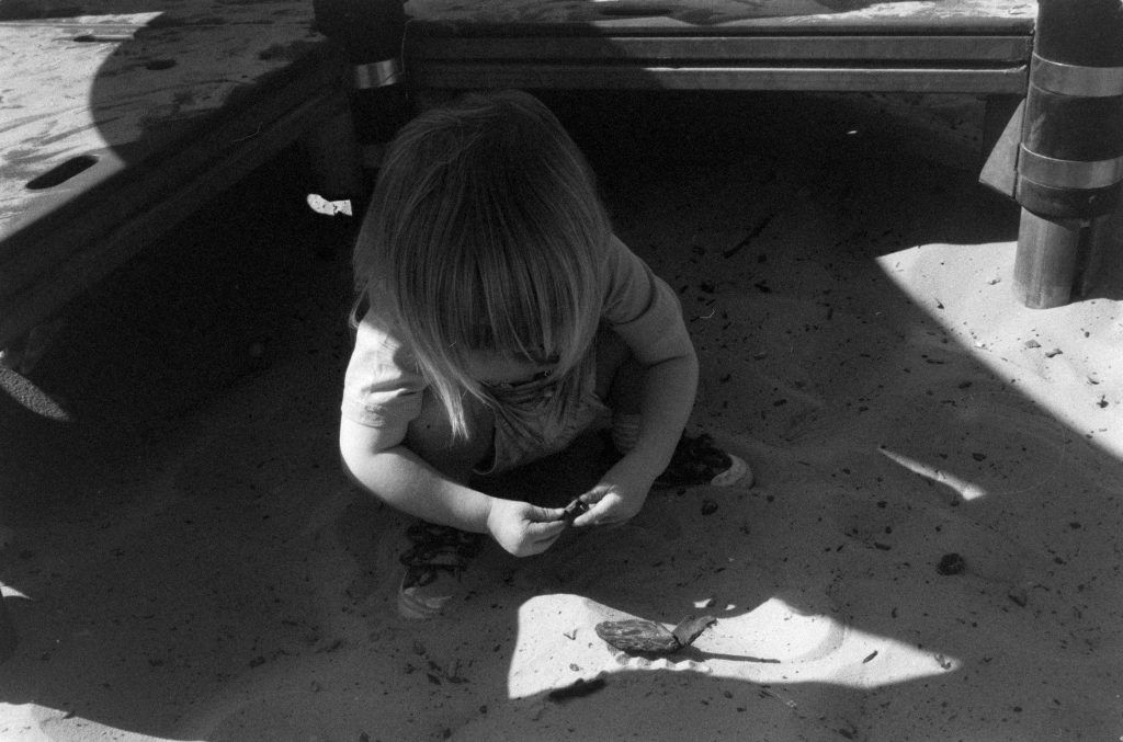 A black and white photo of a small boy playing in a sand pit