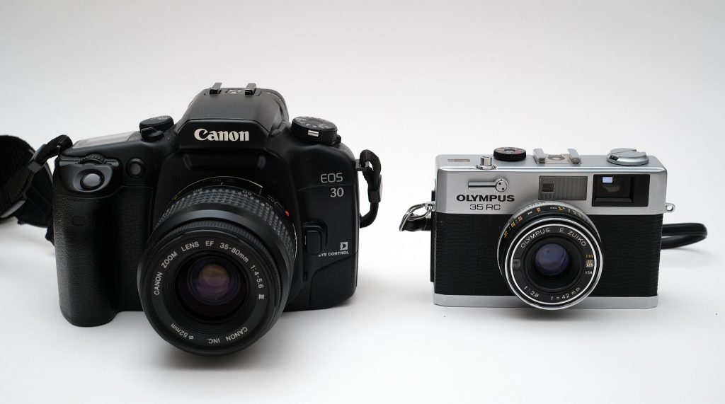 An image of a Canon EOS 30 film SLR next to an Olympus 35RC rangefinder, highlighting the difference in size